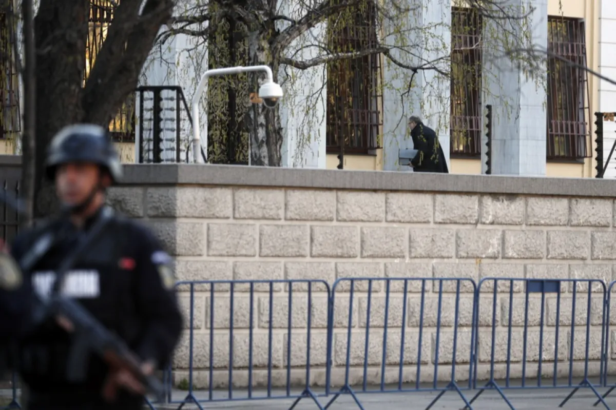 Un bărbat se uită printr-o fereastră din interiorul ambasadei Rusiei în timp ce polițiștii securizează zona din jurul clădirii, în București, România, 6 aprilie 2022.