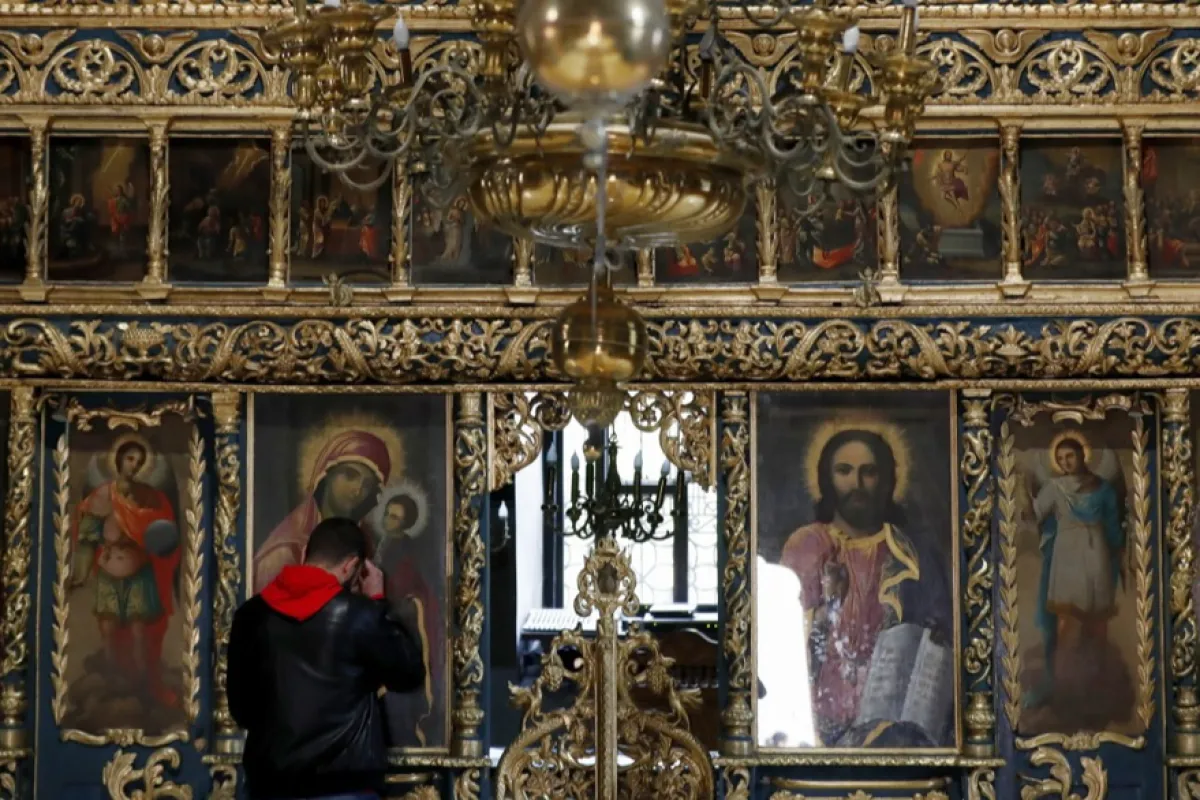 Un pelerin ortodox român se roagă la o icoană care o înfățișează pe Fecioara Maria, în timp ce în afara bisericii este săvârșită o slujbă de Vinerea Mare la biserica ortodoxă Sf. Anton din centrul Bucureștiului, România, 14 aprilie 2023.