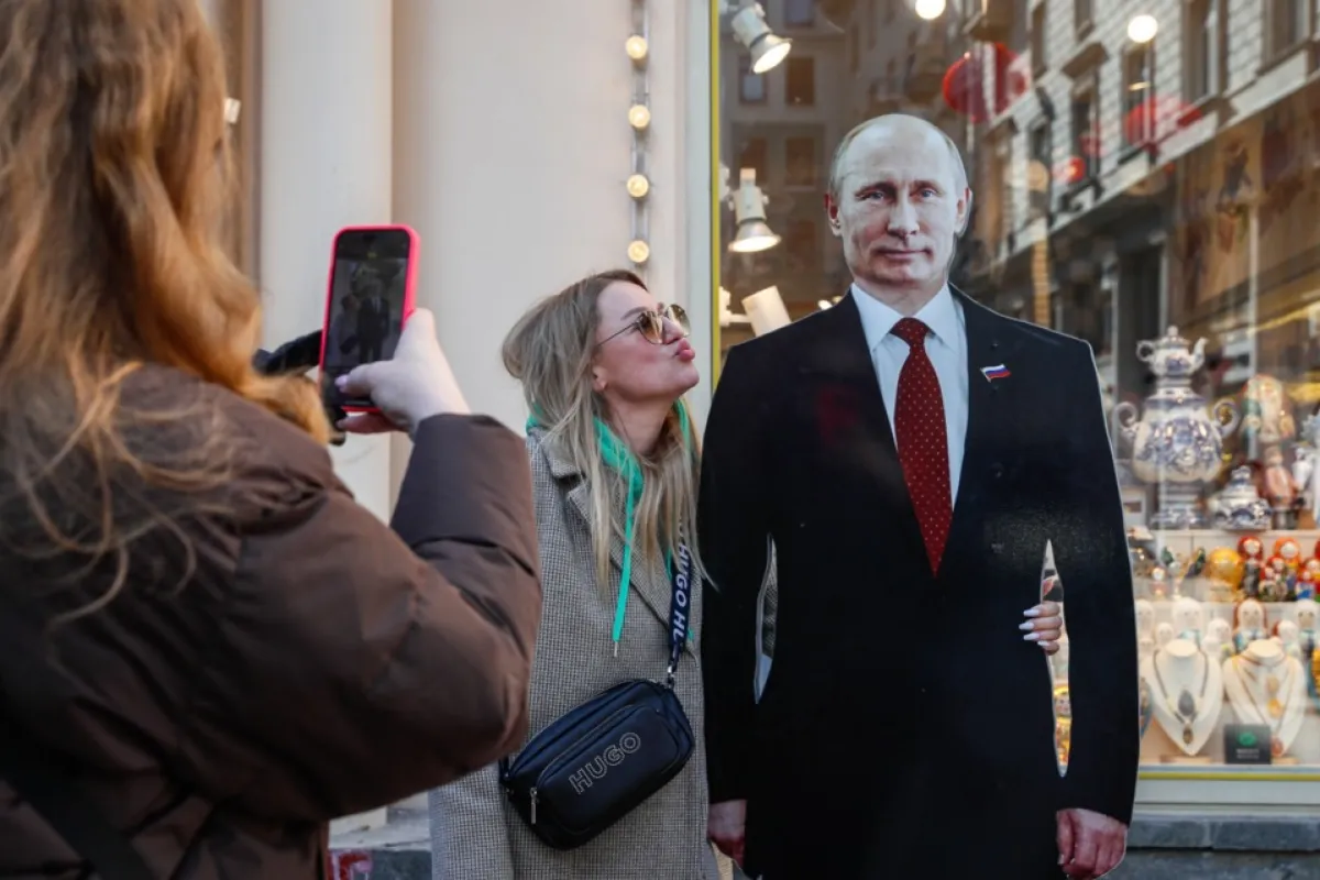 O femeie pozează lângă imaginea de carton a președintelui și candidatului la președinție, Vladimir Putin pe o stradă din Moscova, Rusia, 13 martie 2024.